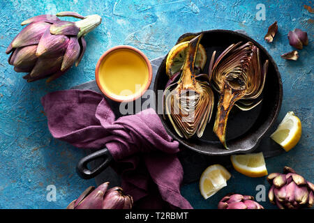 Flat lay with grilled and fresh red artishokes, whole and halved, on textured blue background Stock Photo