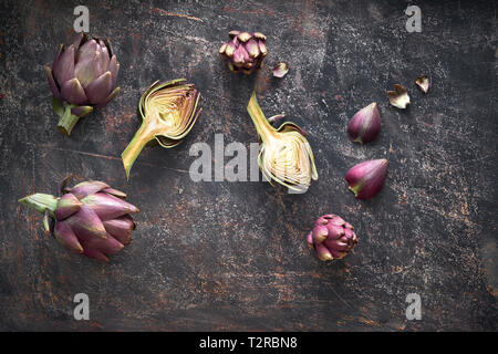 Flat lay with fresh red artishokes, while and halved, on dark background Stock Photo