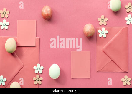 Easter flat lay in coral color with painted eggs, greeting cards, envelopes and decorative flowers Stock Photo