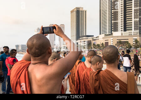 COLOMBO, SRI LANKA - February  19, 2019: A group of buddhist monks with orange clothes looking  the city and taking photos from the Galleface Observat Stock Photo