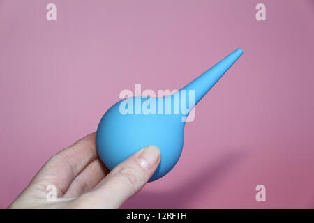 Blue syringe with a soft tip in a female hand. Enema holds a woman. Pink background. Medical enema. Stock Photo