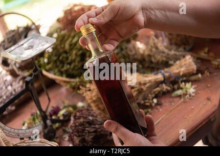 tincture or potion bottle in hand of herbalist  bunch of dry healthy herbs in background alternative medicine Stock Photo