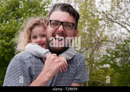 Little girl smiling, hugging her father with her arms around his neck Stock Photo