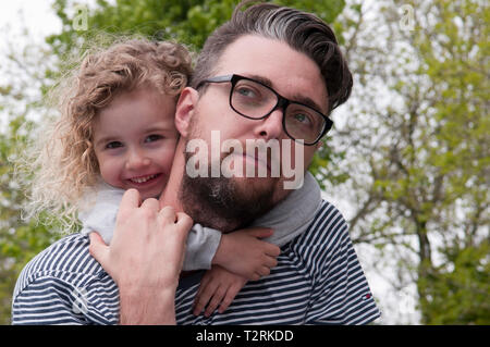 Little girl smiling, hugging her father with her arms around his neck Stock Photo