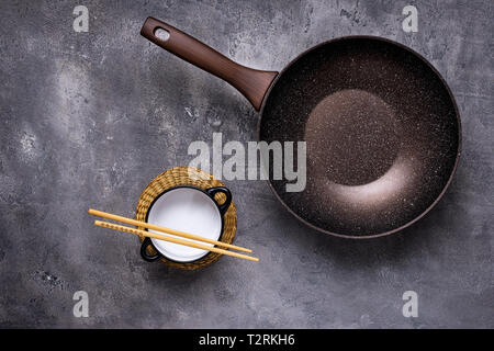 Wok Pan Empty with Wooden Chopsticks on Dark Background. Top View. Stock Photo