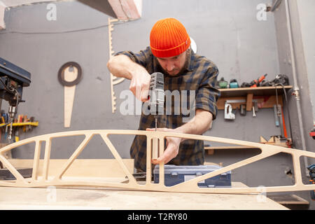 Home repair concepts, close up. Handicraft Carpentry. Cabinet-maker hands drilling a wooden plank using screwdriver on the working table in the worksh Stock Photo