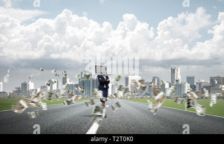 Business woman in suit with laptop instead of head keeping arms crossed while standing on the road among flying dollar banknotes with beautiful landsc Stock Photo