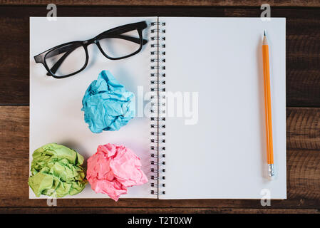Eyeglasses, crumpled paper and blank spiral notebook with copy space on a wooden table. Concept of school, writing, sketching and workspace. Stock Photo