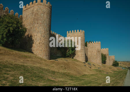 Lined stone towers on the large city wall in Romanesque style and green lawn at Avila. With an imposing wall around the gothic city center in Spain. Stock Photo