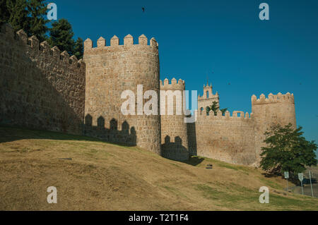 Lined stone towers on the large city wall in Romanesque style and green lawn at Avila. With an imposing wall around the gothic city center in Spain. Stock Photo