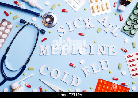 Cold medicine, thermometer, phonendoscope and words: sick, ail, medicine, cold and flu, on a blue background. Cold and Flu Treatment Stock Photo