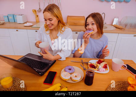 Family breakfast. Beaming freelancer enjoying family breakfast with her cute teenage sibling Stock Photo