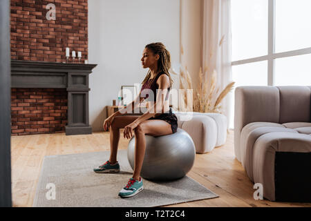 Exercising on ball. Young slim and fit businesswoman exercising on fitness ball at home in the morning
