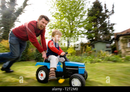 Father pushing his son on a toy tractor in their back garden Stock Photo