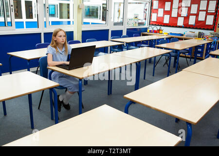 Schoolgirl sitting at a desk in an empty elementary school classroom ...