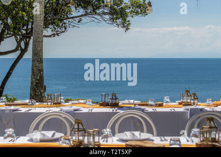 Set white tables for wedding dinner decorated in Mediterranean style. View of the ocean. Concept of a tropical destination wedding. Stock Photo