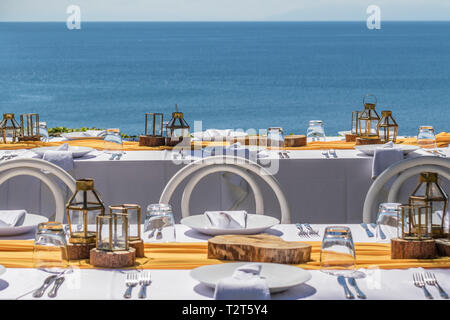 Set white tables for wedding dinner decorated in Mediterranean style. View of the ocean. Concept of a tropical destination wedding. Stock Photo