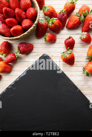 Strawberries copy space with a small basket of strawberries surrounded by strawberries scattered on a wooden bottom and a plate of slate taken from ab Stock Photo