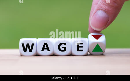 Symbol for a salary increase. Hand turns a dice and changes the direction of an arrow from down to up. Dice form the word 'wage'. Stock Photo