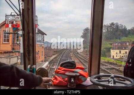 At the controls: train driver's view through front window of moving diesel train on heritage railway line. Leaving vintage station. Stock Photo