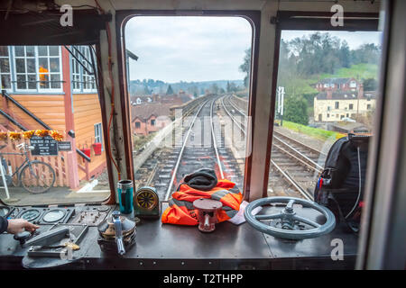At the controls, in the driving seat. Train driver view through front window of moving diesel train on heritage railway line. Leaving vintage station. Stock Photo