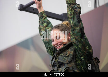 04 April 2019, North Rhine-Westphalia, Köln: Marion Gregor tries her hand at a chin-up on a course at the Bundeswehr stand at the Fibo fitness trade fair. Fibo is the world's largest trade fair for fitness, wellness and health. More than 1,100 exhibitors from Europe and other regions of the world will be presenting their innovations. Photo: Rolf Vennenbernd/dpa Stock Photo