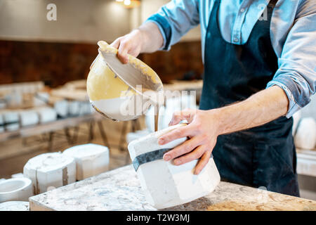 Worker pouring special liquid into the gypsum form making ceramic products at the pottery manufacturing, close-up view Stock Photo