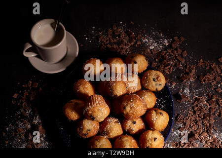 group of muffins with chocolate on a blue plate next to a cup of milk Stock Photo
