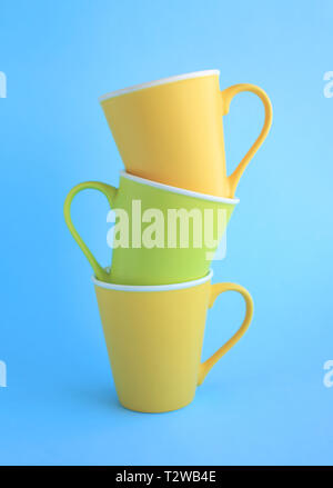 Three colorful yellow and light green ceramic cups on light blue background. Stock Photo