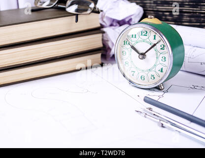 Several tools for drawing, glasses and retro clock lying in the drawings. Architectural prints and print rolls and a drawing instruments on the workta Stock Photo