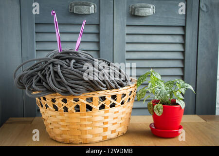 Traditional colorful yarns for hobby knitting in a straw eco basket on a light wooden surface, knitting needles, flower in a red pot. Stock Photo