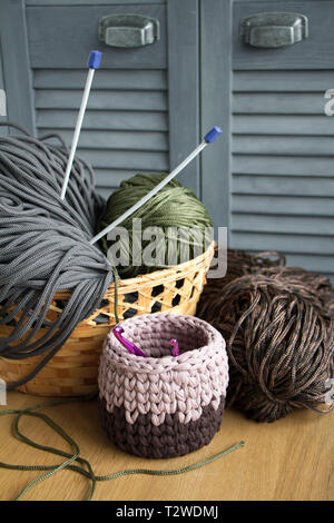 Traditional colorful yarns for hobby knitting in a straw eco basket on a light wooden surface, knitting needles, knitted basket. Stock Photo