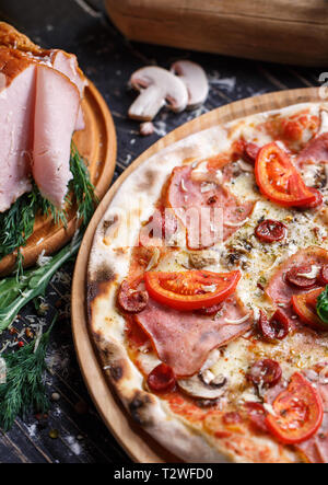 Pizza with sausages, ham, mushrooms and tomatoes. Background ready for your design. Pizza on a black background Stock Photo