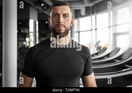 Bearded man professional personal trainer standing at gym looking camera smiling confident close-up Stock Photo