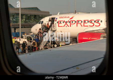 Iberia Express Airbus A320 jet plane at Dublin Airport and passengers people boarding commercial flight as seen through an airplane window