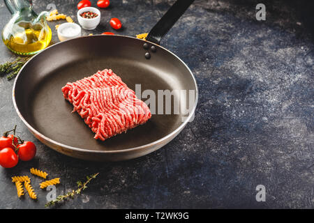 Fresh raw minced beef in frying pan and ingredients over dark background. Top view or flat-lay. Stock Photo