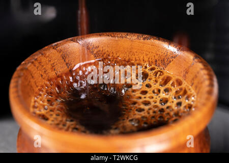 A coffee is being prepared in a small wooden cup by a coffee machine. Stock Photo