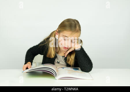 Portrait of a cute girl is reading a book, doing homework. She can do this at home or school Stock Photo