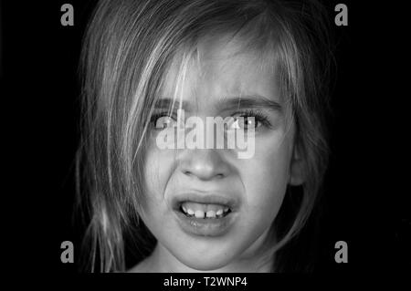 Portrait of a young girl, shows disgusted emotion on a black background in black and white Stock Photo