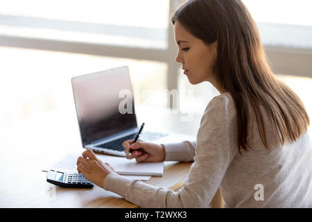 Side rear view young female sitting at table calculating money Stock Photo