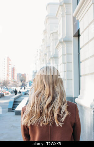 Stylish fashionable woman wearing coat with curly blonde hair at the street