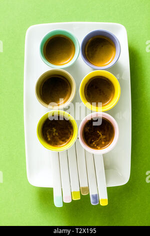 Six multicolored cups of Italian espresso coffee with porcelain spoons on a serving plate. on a green background. Stock Photo