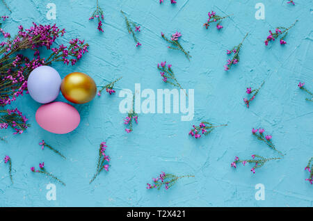 Three Easter eggs with heather flowers on blue background. Flat lay. Top view. Stock Photo