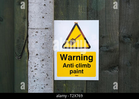 Bright yellow sign Warning Anti-climb paint mounted on wooden fence Stock Photo