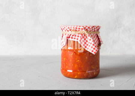 Vegetable sauce adjika with tomatoes, garlic, bell peppers in jar on light background. Space for text. Stock Photo
