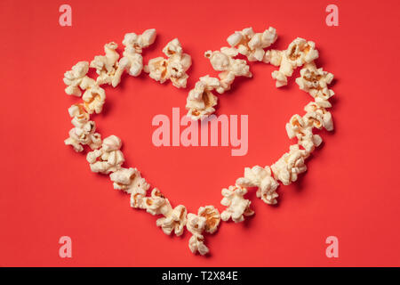Love cinema concept of popcorn. Heart shaped white fluffy popcorn on red background with empty space for text Stock Photo