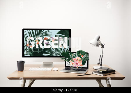 computer with green lettering and monstera leaves illustration on monitor on wooden table Stock Photo