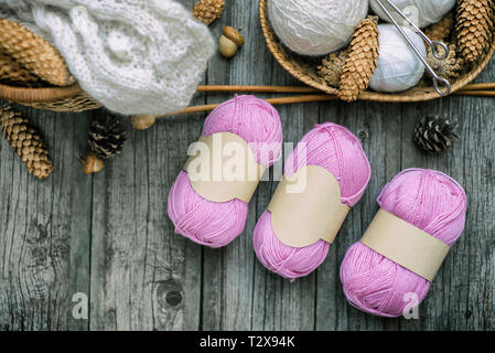 Three pink balls of wool threads with empty labels lying on vintage wood desk with knitting needles and basket. Mock up background for your craft knit Stock Photo