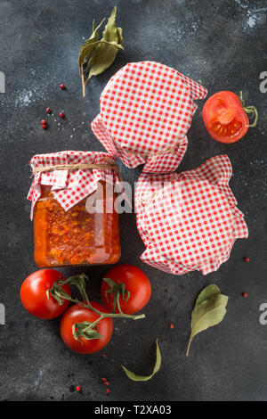 Homemade vegetable adjika in jar on black background. Made of tomatoes, garlic, bell pepper and spice. Close-up Stock Photo