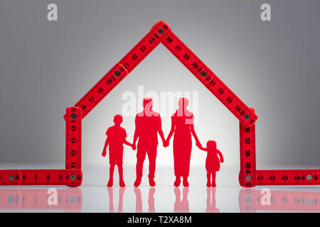 Family Holding Hands Under The House Made With Red Measuring Tape On Desk Stock Photo